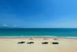 A beach with four sun loungers and umbrellas, a clear sky, and calm sea. - Fusion Resort Cam Ranh (Cam Lam)
