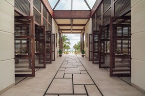 A corridor with wooden lattice partitions, potted plants, and a view of palm trees through the open end. - Fusion Resort Cam Ranh (Cam Lam)
