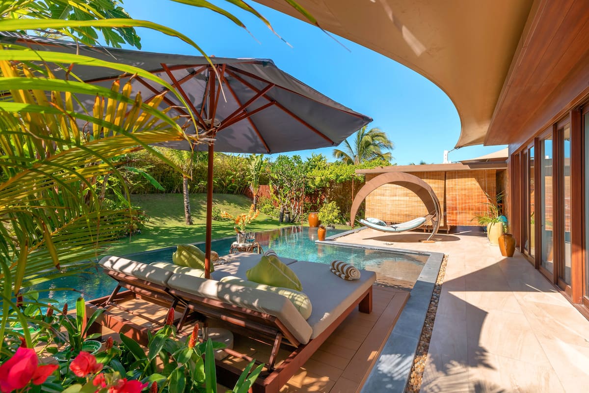 Ein Poolbereich mit Liegestühlen, Sonnenschirm und Blick auf Pool und Garten.