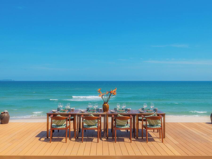 A wooden deck with a table set for six, overlooking the ocean.