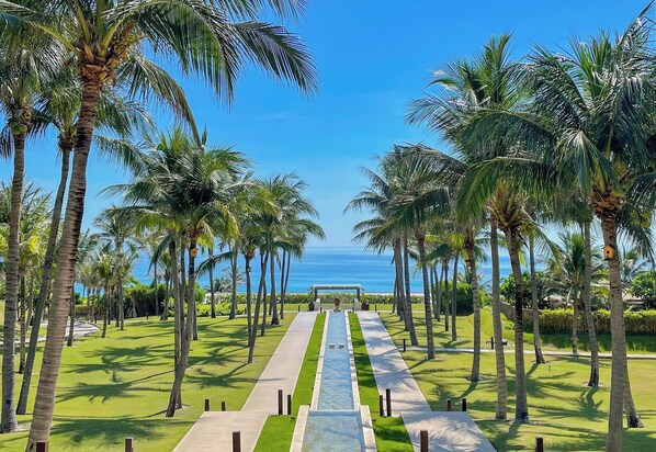 A pathway lined with palm trees leading to a view of the ocean. - Fusion Resort Cam Ranh (Cam Lam)