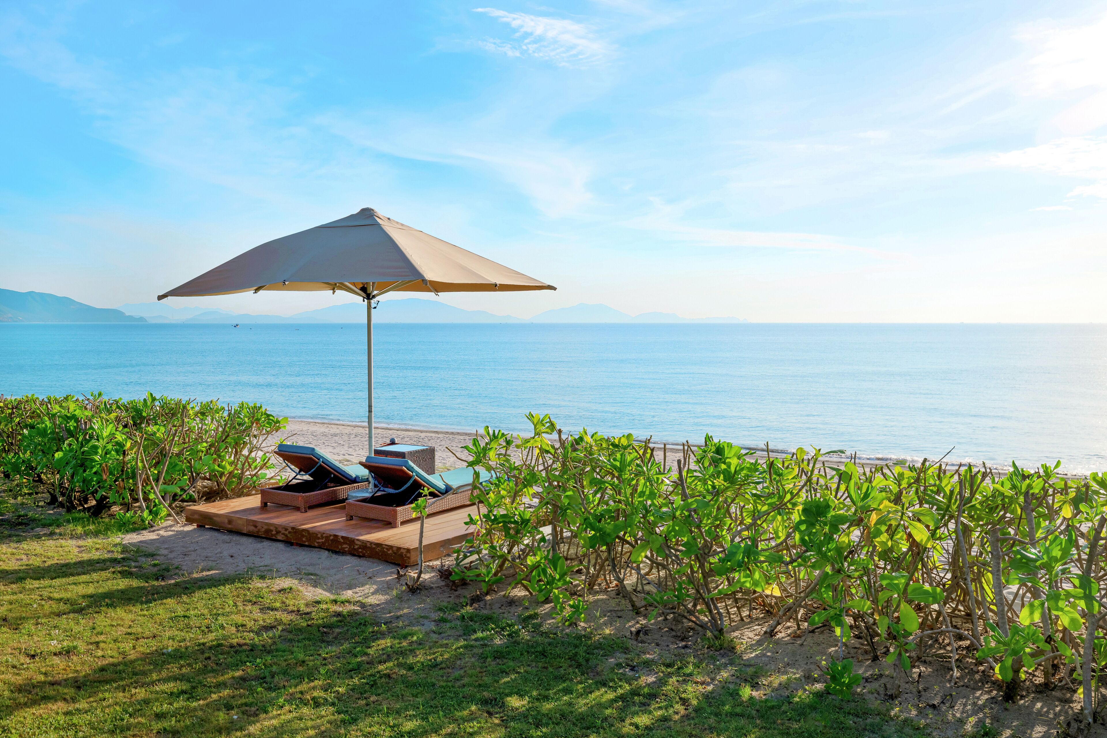A beachside lounge area with a large umbrella, lounge chairs, and a view of the sea.
