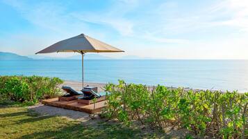 A beachside lounge area with a large umbrella, lounge chairs, and a view of the sea.