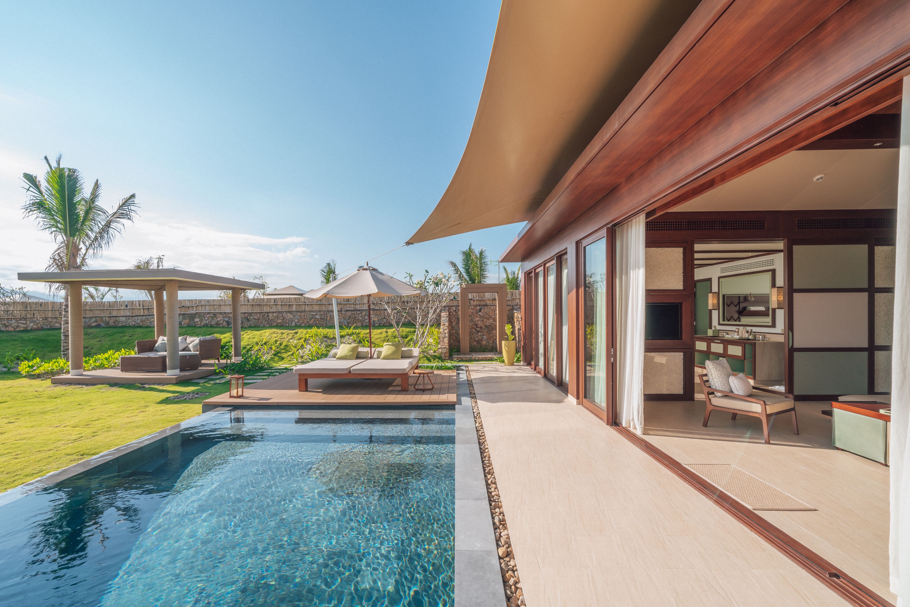 Un área de piscina moderna al aire libre con sillones de descanso, una pérgola y vistas de la propiedad.
