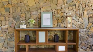 A wooden console table with a stone wall backdrop, featuring a framed inspirational quote, two vases, and a lantern.
