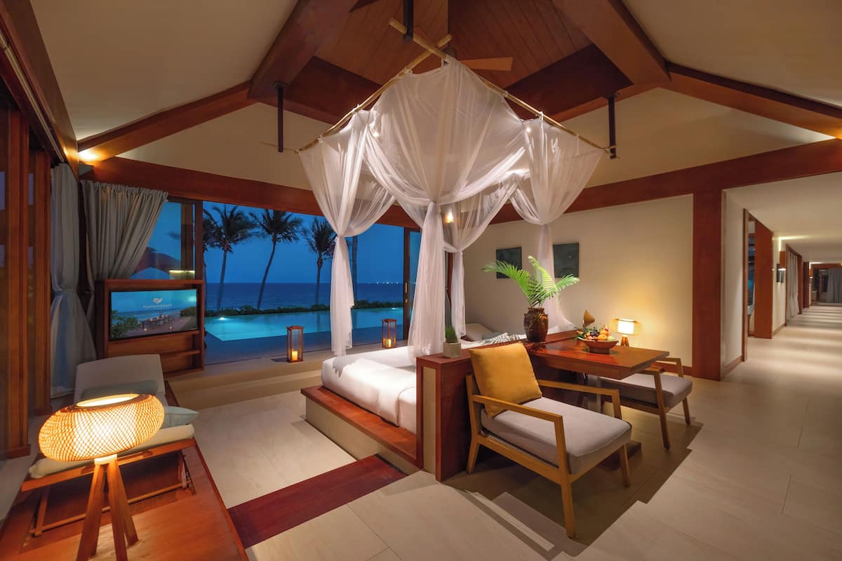 Ein luxuriöses Schlafzimmer mit Baldachinbett, Schreibtisch mit Lampe und Meerblick.