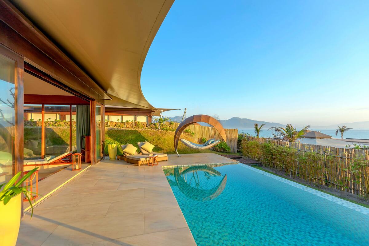 Ein moderner Poolbereich mit Blick auf den Ozean, einer Hängematte und einer Sitzecke mit Kissen.