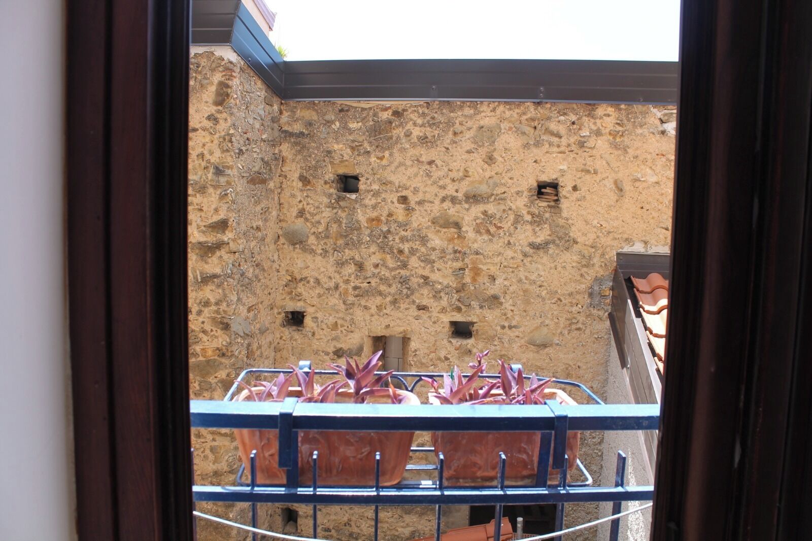 A balcony with potted plants and a stone wall in the background.