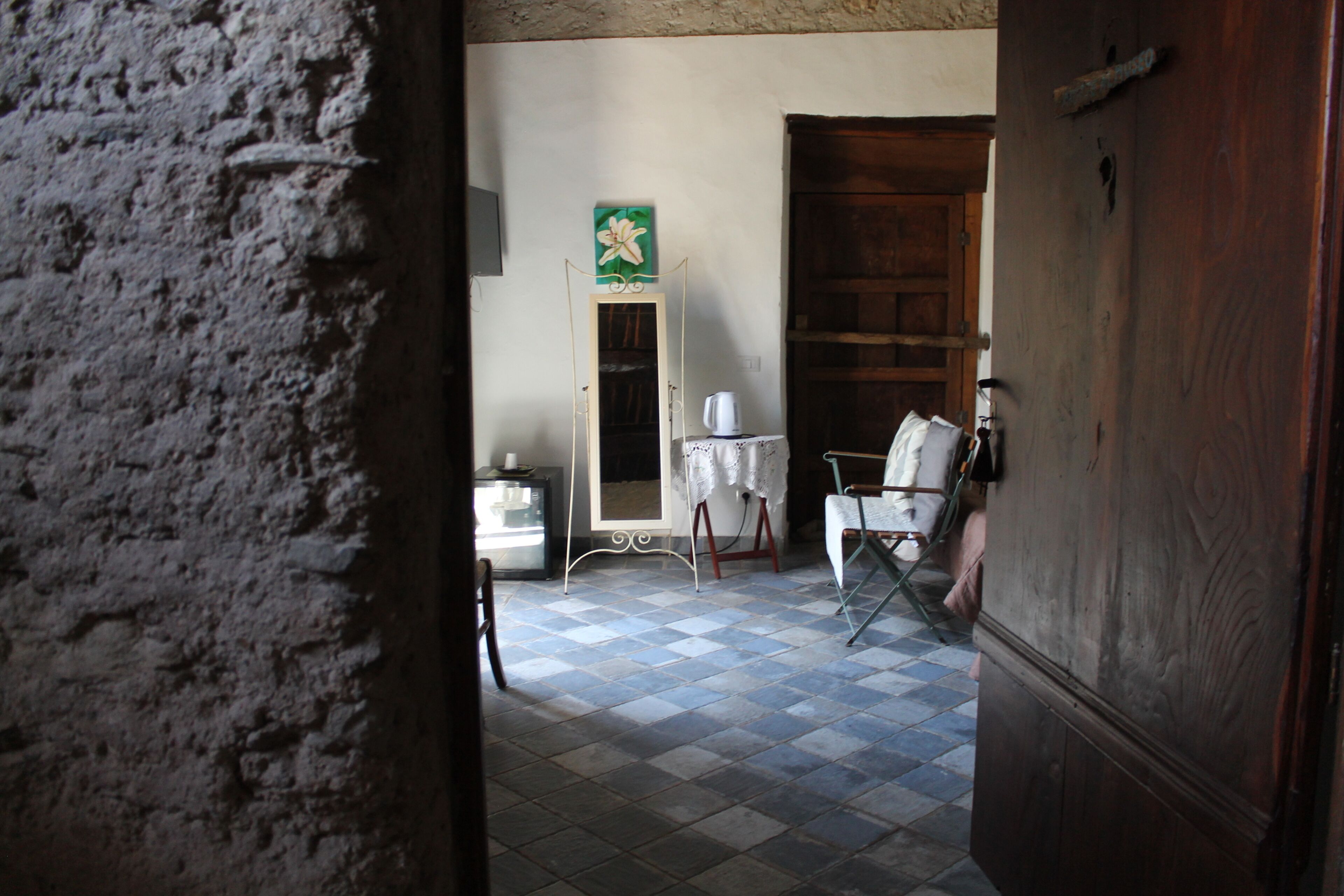 A room with a checkered floor, a wooden door, a mirror, a chair, and a table.