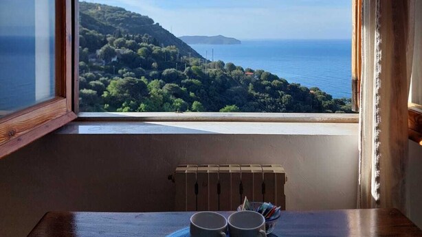 A room with a view of a coastal landscape, a table with two cups and a plate, and a radiator. - La Casa sul Blu Albergo Diffuso (Pisciotta)