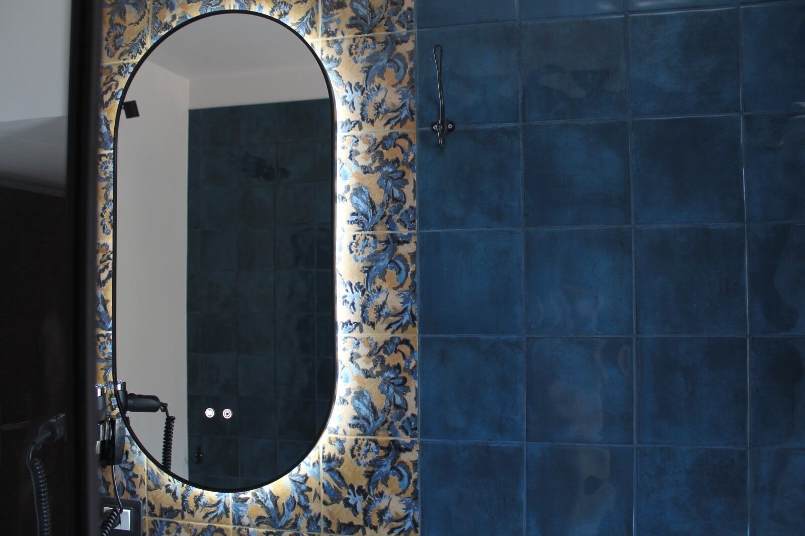 Un baño con un espejo redondo, azulejos azules y un estampado floral en la pared.