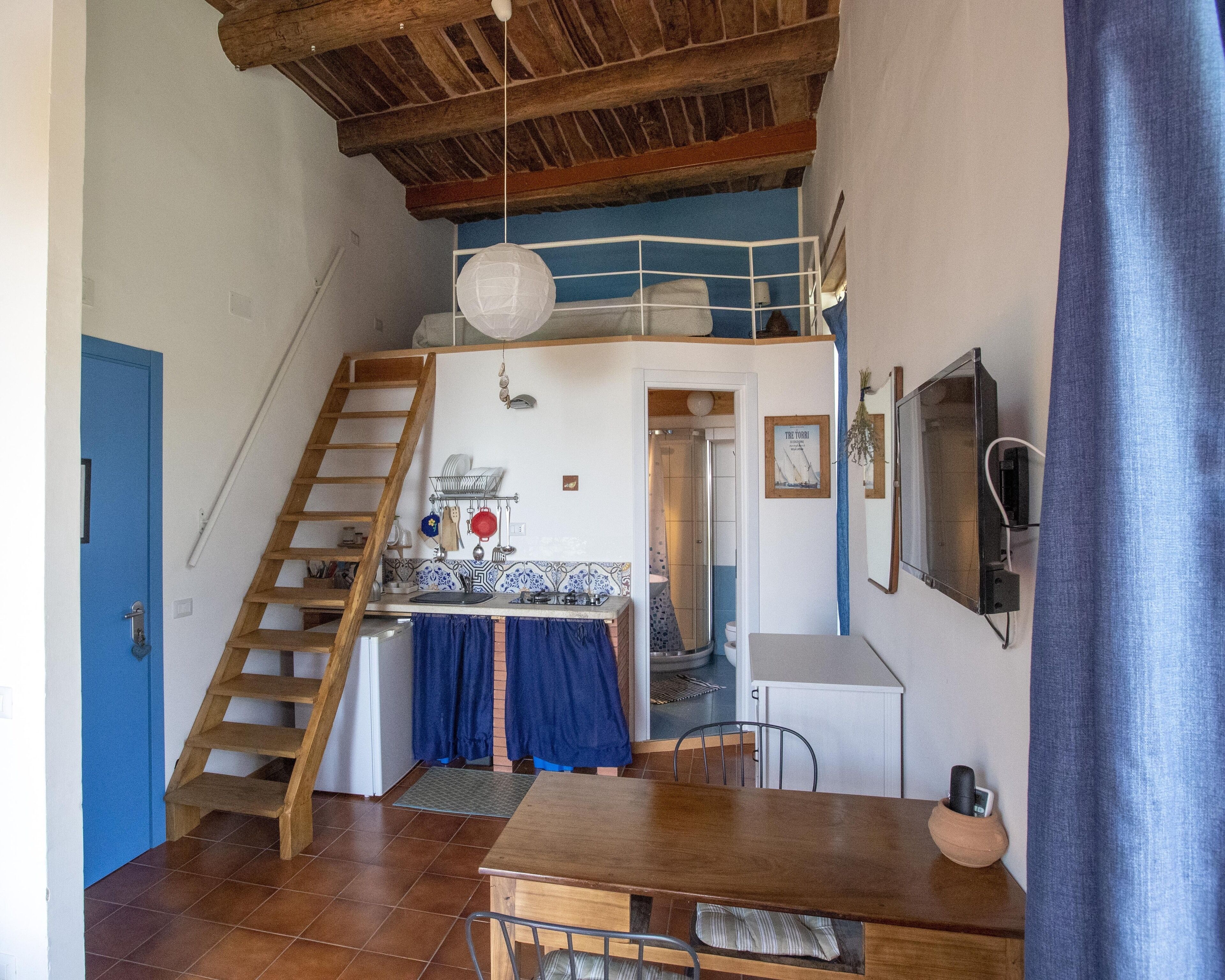 Une cuisine compacte avec un escalier en bois, un coin repas avec une table et des chaises, et une porte bleue.