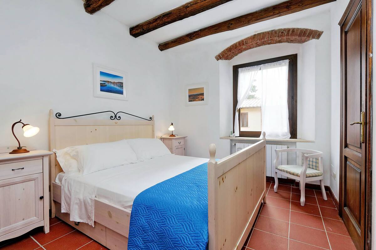 Une chambre à coucher comprenant un lit, une table de chevet, une lampe, une chaise et une fenêtre donnant sur un paysage agréable.