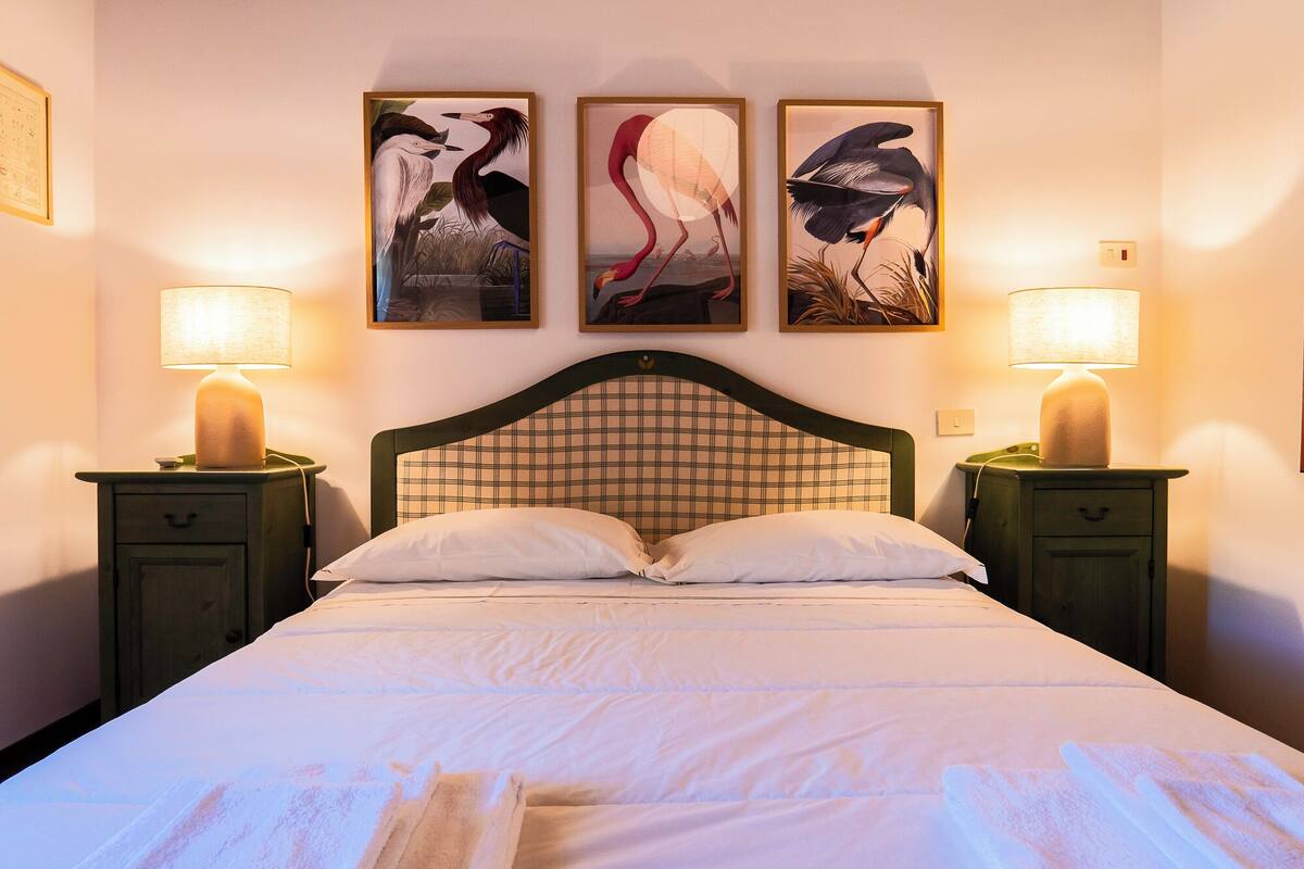 Une chambre d’hôtel avec un lit, deux tables de chevet avec des lampes et trois tableaux représentant des oiseaux, encadrés et accrochés au mur.