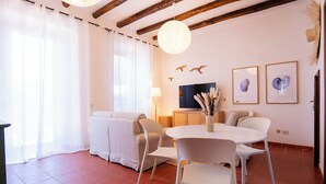Een moderne woonkamer met een ronde eettafel, witte stoelen, een bank, een flatscreen televisie en decoratieve muurkunst.