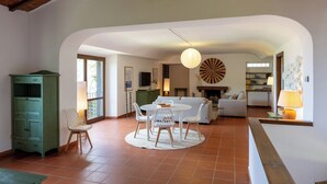 Een ruime woonkamer met een ronde eettafel, witte stoelen, een bank en een dartbord aan de muur.