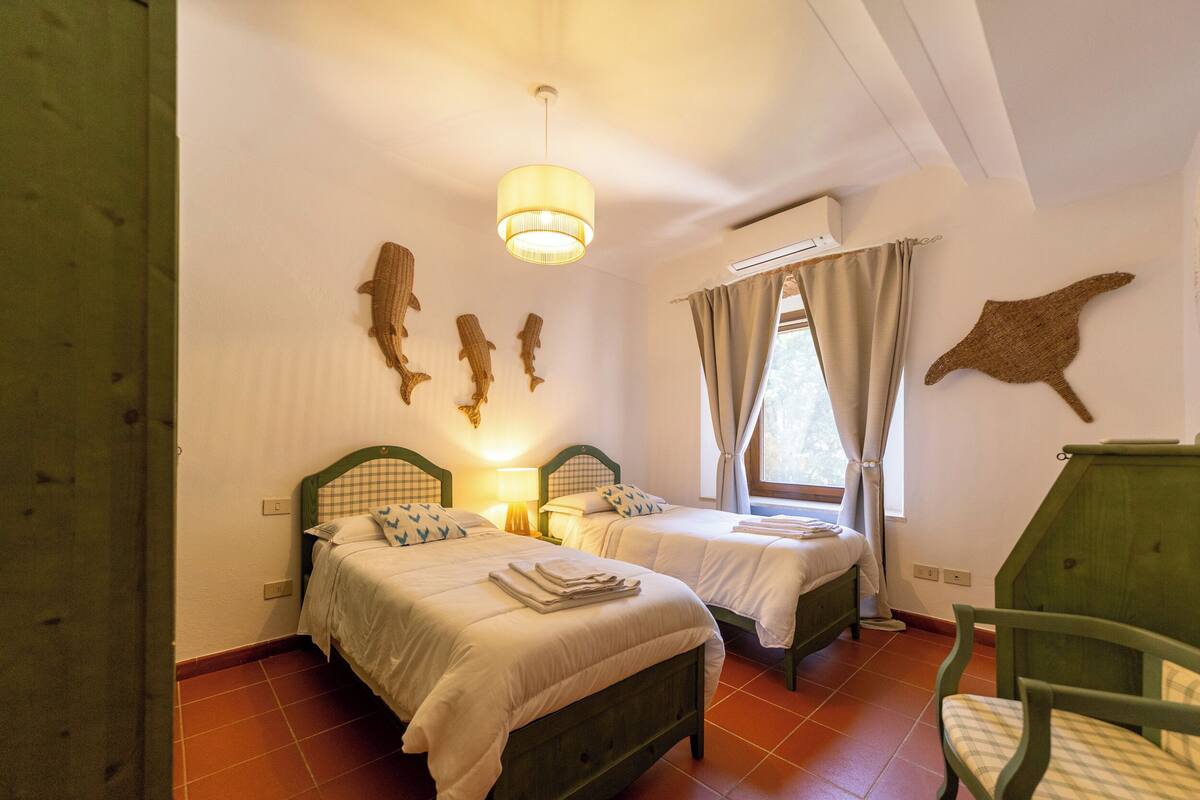 Une chambre avec deux lits, un luminaire suspendu, un climatiseur fixé au mur et une chaise.