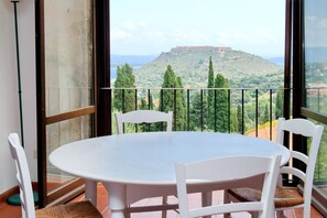 A balcony with a white table and chairs, overlooking a hill with a fort-like structure. - Agriturismo Pimpinnacolo (Monte Argentario)