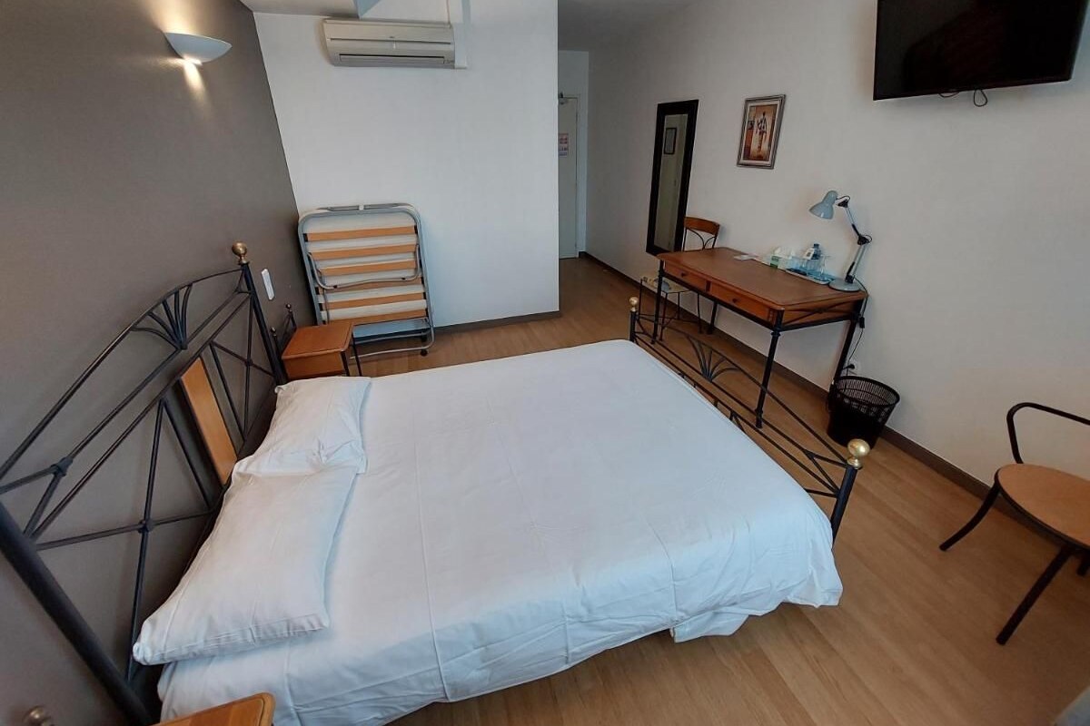 A bedroom with a bed, a desk, a chair, a TV, and an air conditioning unit.
