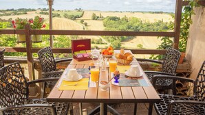A wooden table set with breakfast items, including croissants and orange juice, on a balcony with a scenic view of fields. - Hotel Le Relais Des Deux Vallees (Salvagnac)