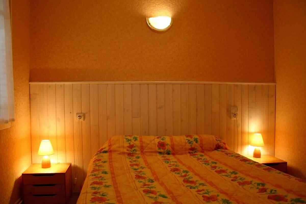 Une chambre à coucher avec une tête de lit en bois, deux tables de chevet avec des lampes et une couvre-lit à motifs floraux.