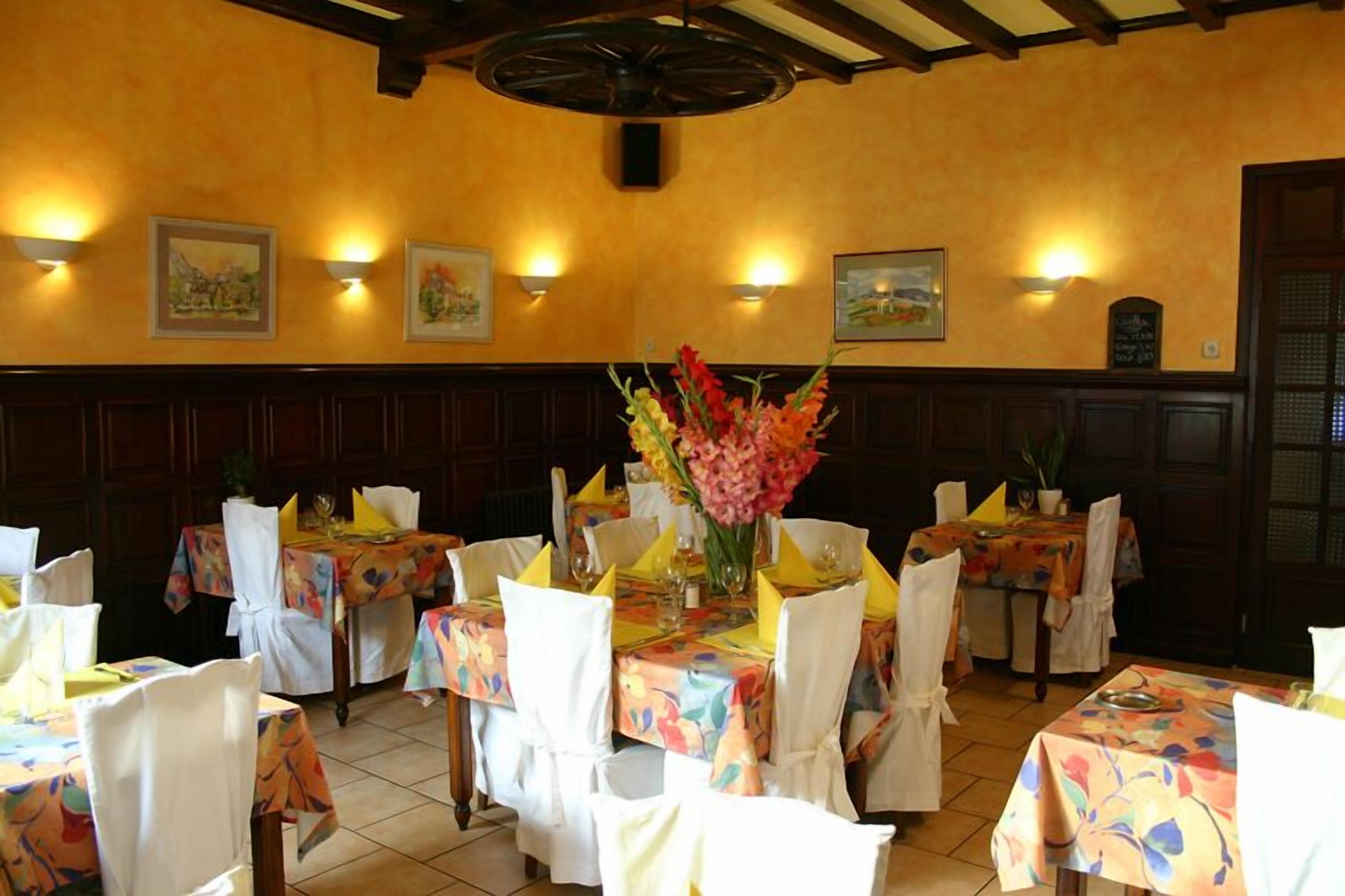 Un restaurant où les tables sont dressées pour le service, avec des nappes à motifs floraux et des chaises blanches.