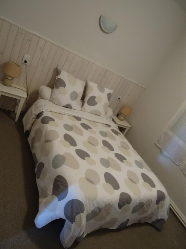 Un dormitorio con cama, dos mesitas de noche y una lámpara fijada a la pared.