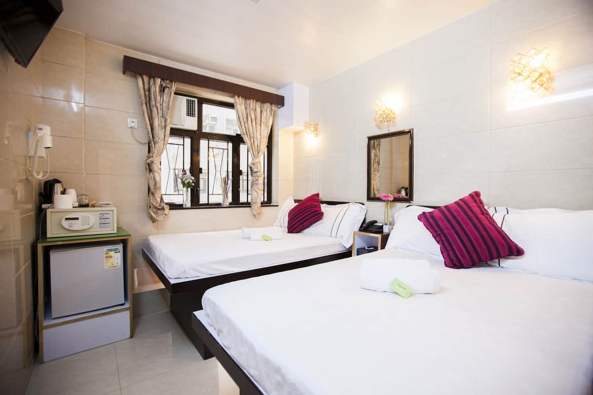 A hotel room with two beds, a small desk with a telephone and a radio, and a window with curtains.