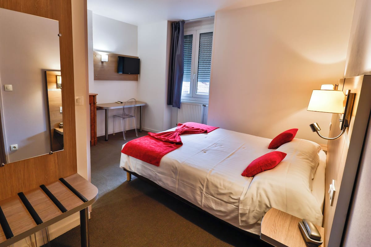 A hotel room with a bed, a desk, a chair, a TV, and a window with curtains.