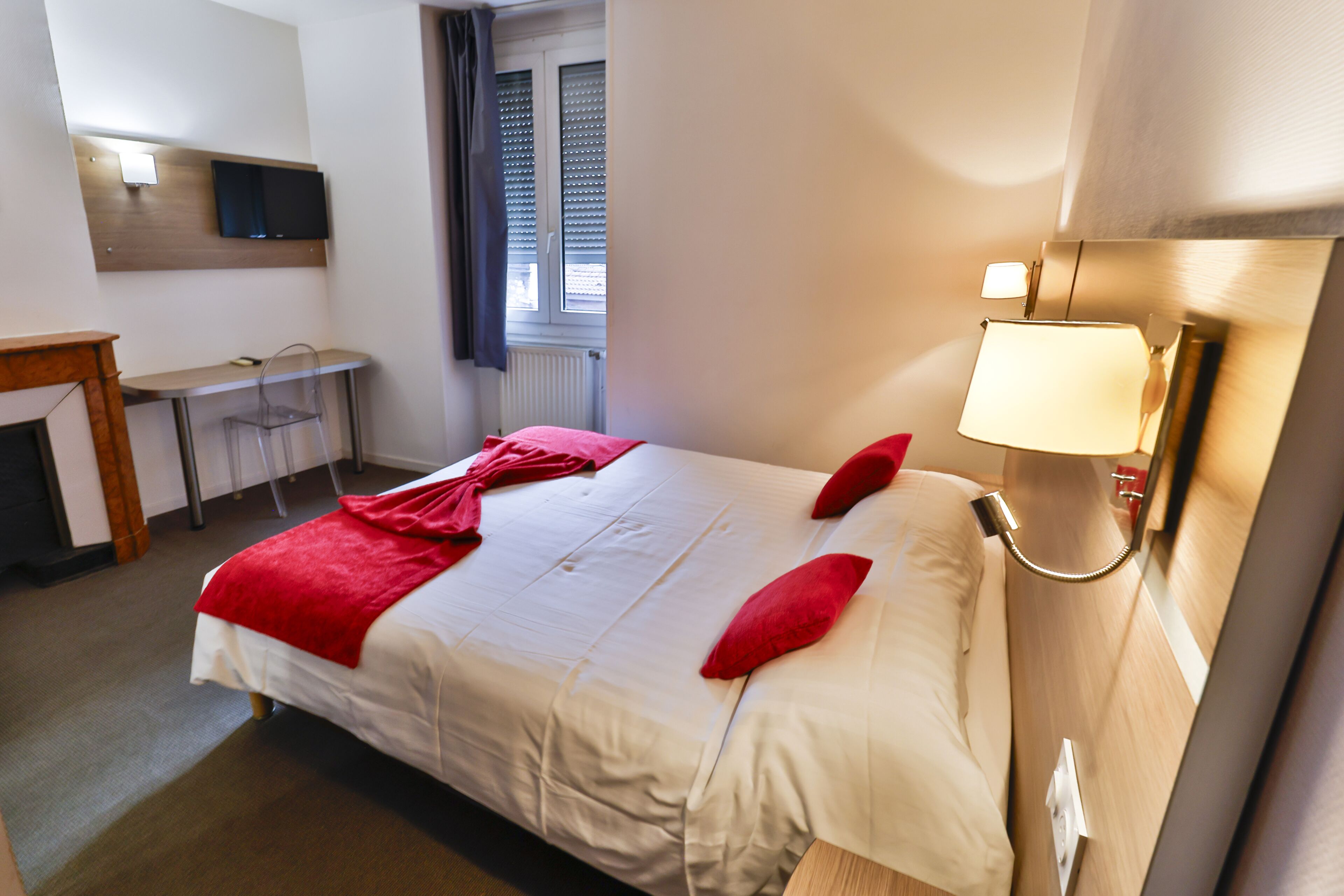 A hotel room with a bed, a desk, a chair, a TV, and a window with blinds.
