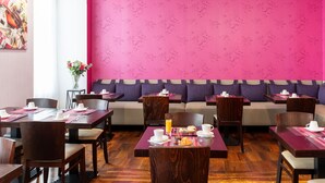 A restaurant with wooden tables and chairs, a pink wall with a floral pattern, and a seating area with purple cushions. - Hôtel de l'Europe Grenoble Hyper Centre (Grenoble)