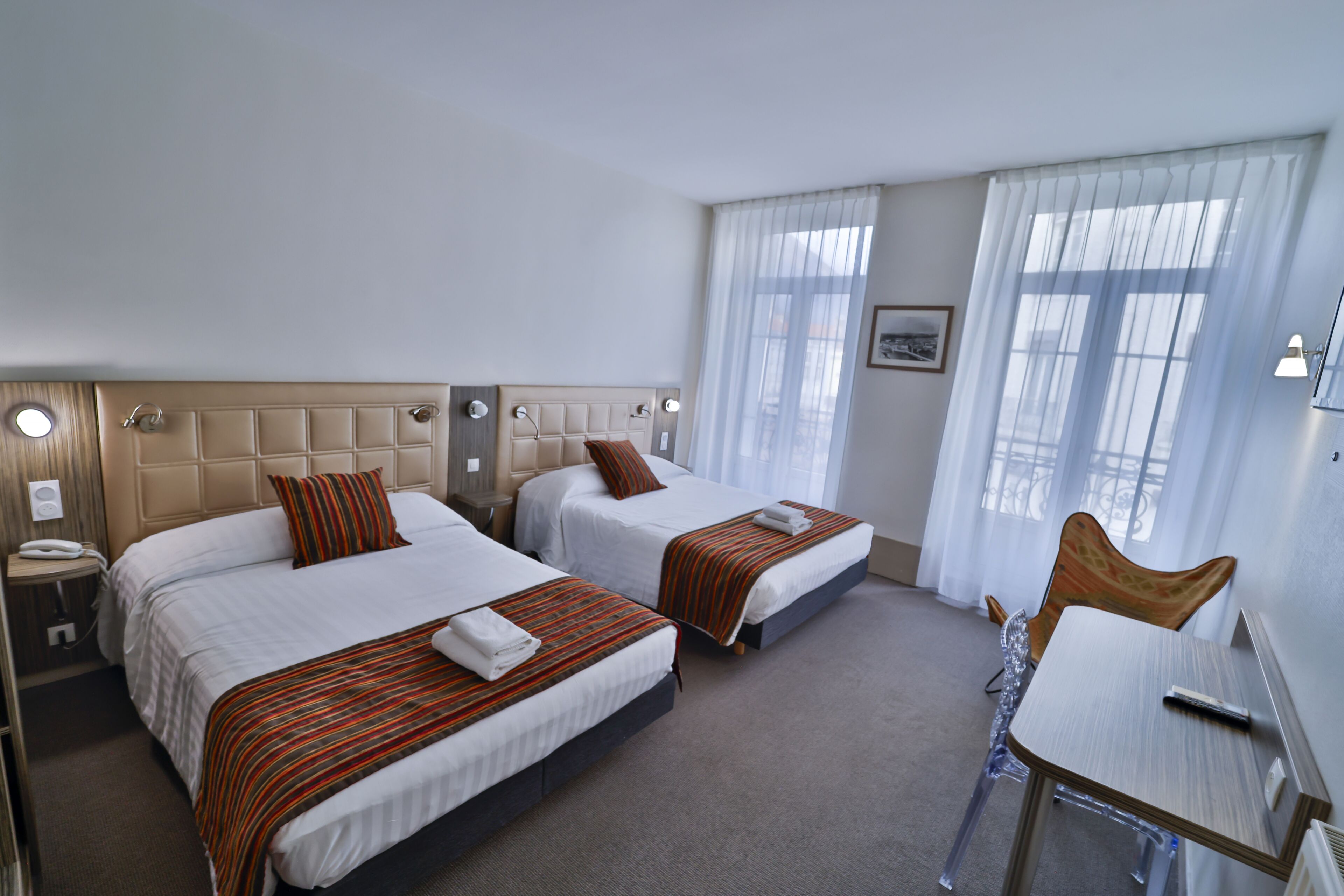 A hotel room with two beds, a desk, and a chair.