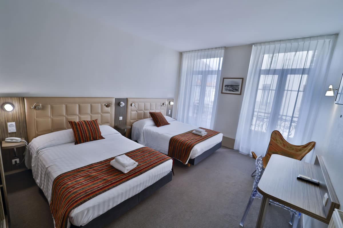 A hotel room with two beds, a desk, and a chair.