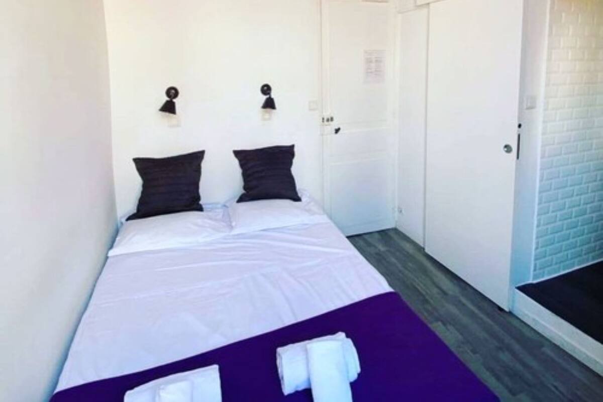 A room with a bed, white walls, a purple ceiling, and a white door.