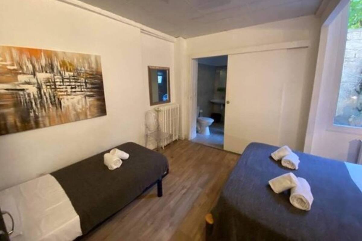 A room with two beds, a painting on the wall, and a view of a bathroom.