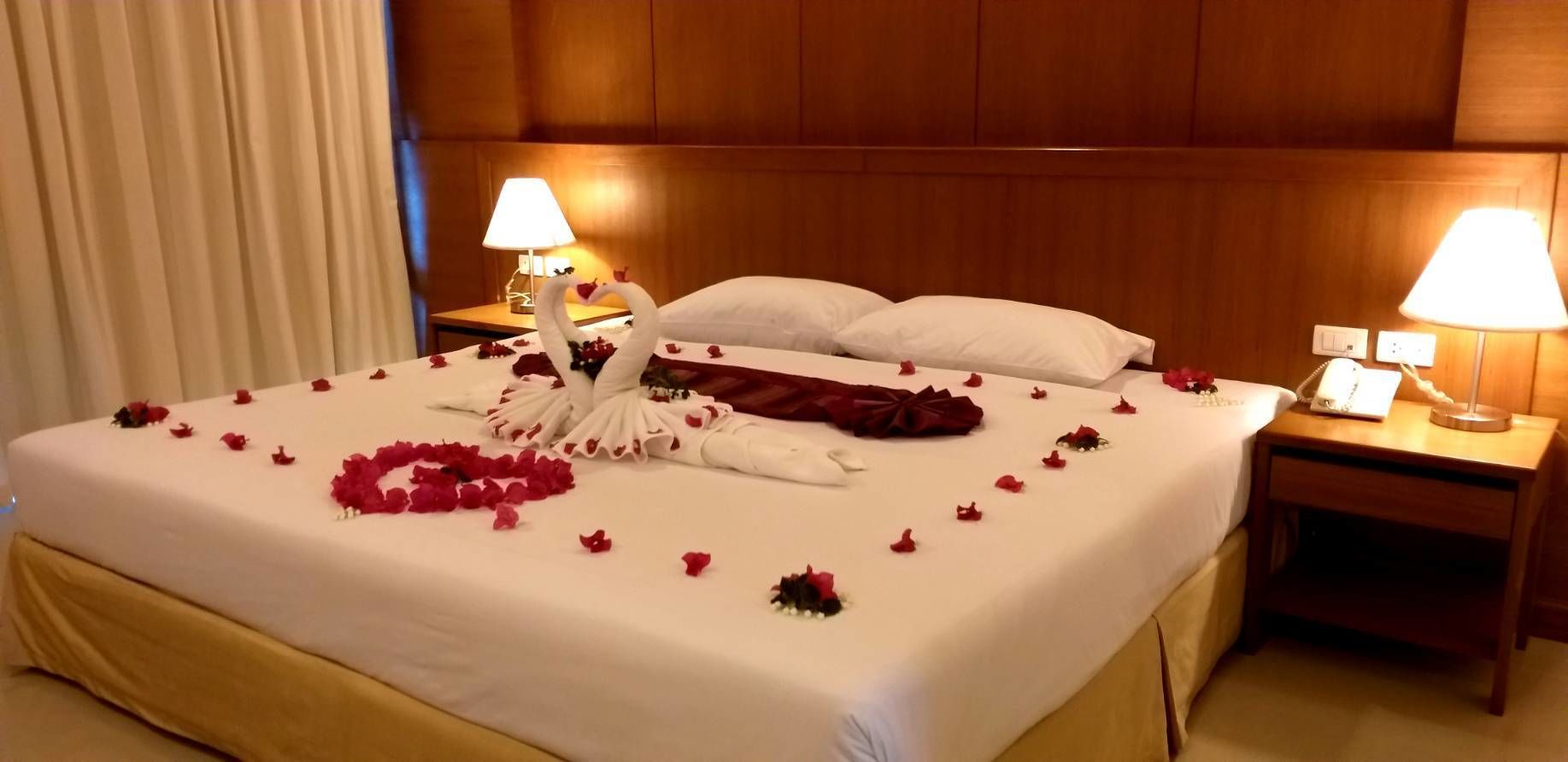A hotel room with a neatly made bed, two bedside lamps, and a wooden headboard.