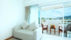 A hotel room with a white sofa, a wooden chair, and a small table with fruit. - Rawai Princess Hotel (Rawai)