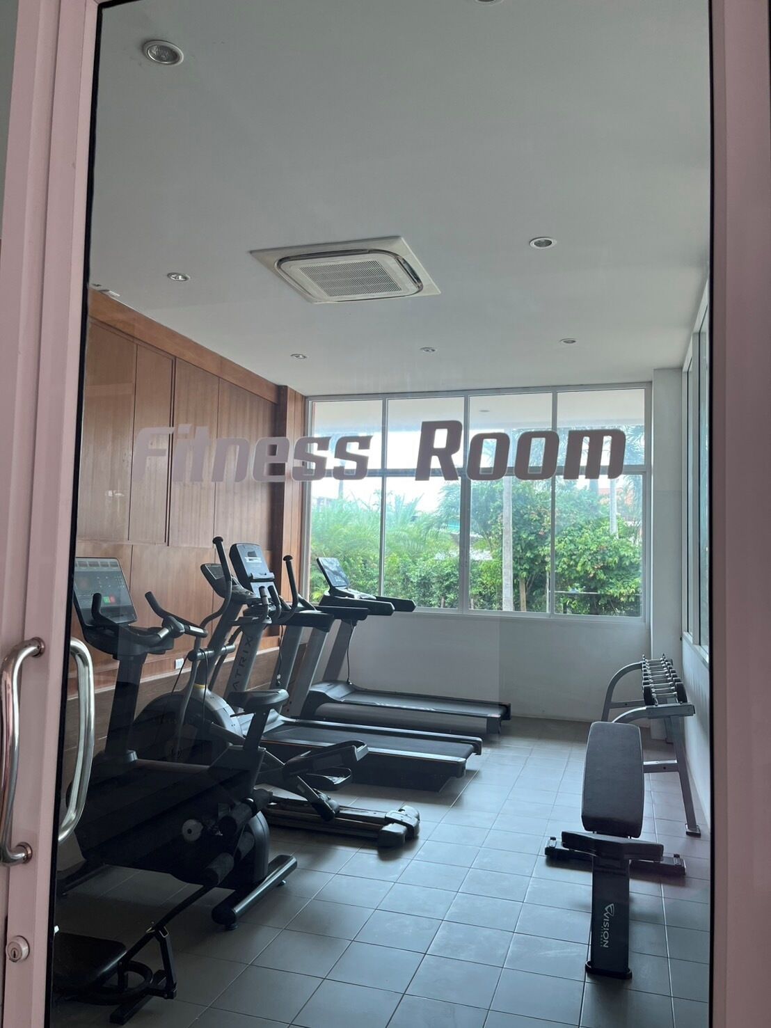 A fitness room with treadmills, a bench, and a window with a view of greenery.