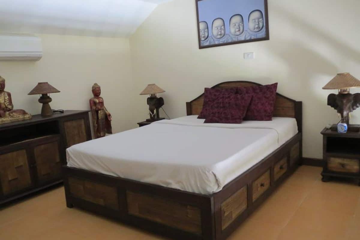 A bedroom with a wooden bed, a nightstand with a lamp, a wall-mounted picture, and a statue on the nightstand.