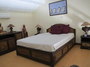 A bedroom with a wooden bed, a nightstand with a lamp, a wall-mounted picture, and a statue on the nightstand.
