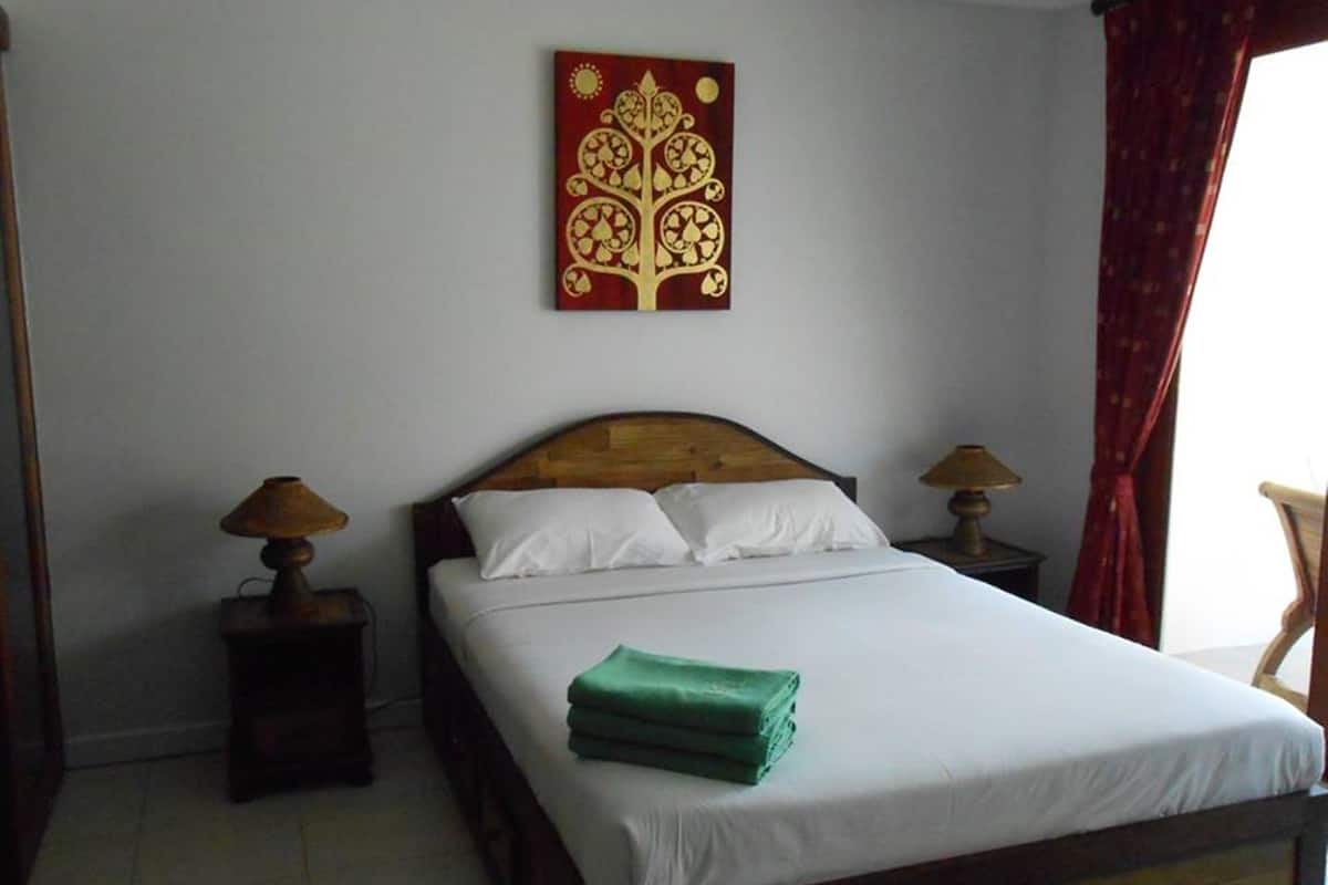 A neatly made bed with white linens, a green towel, two bedside lamps, and a wall art piece above the bed.