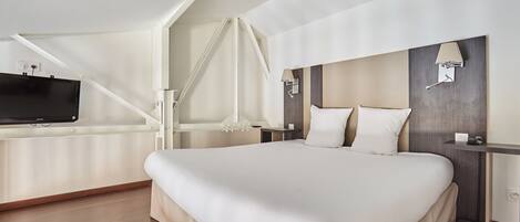 A modern hotel room with a large bed, a TV mounted on the wall, a desk with a lamp, and a wooden floor.