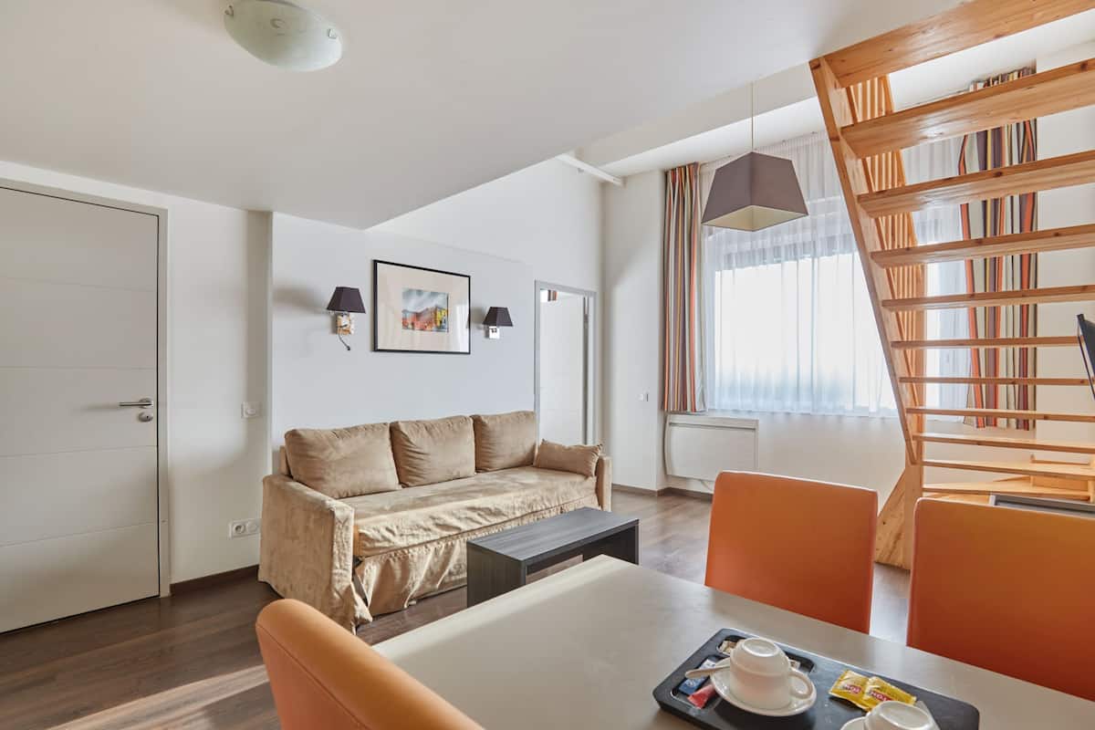Une chambre dâhĂŽtel moderne avec un canapĂ©, une table Ă manger et des chaises, une bibliothĂšque et une fenĂȘtre avec des rideaux.