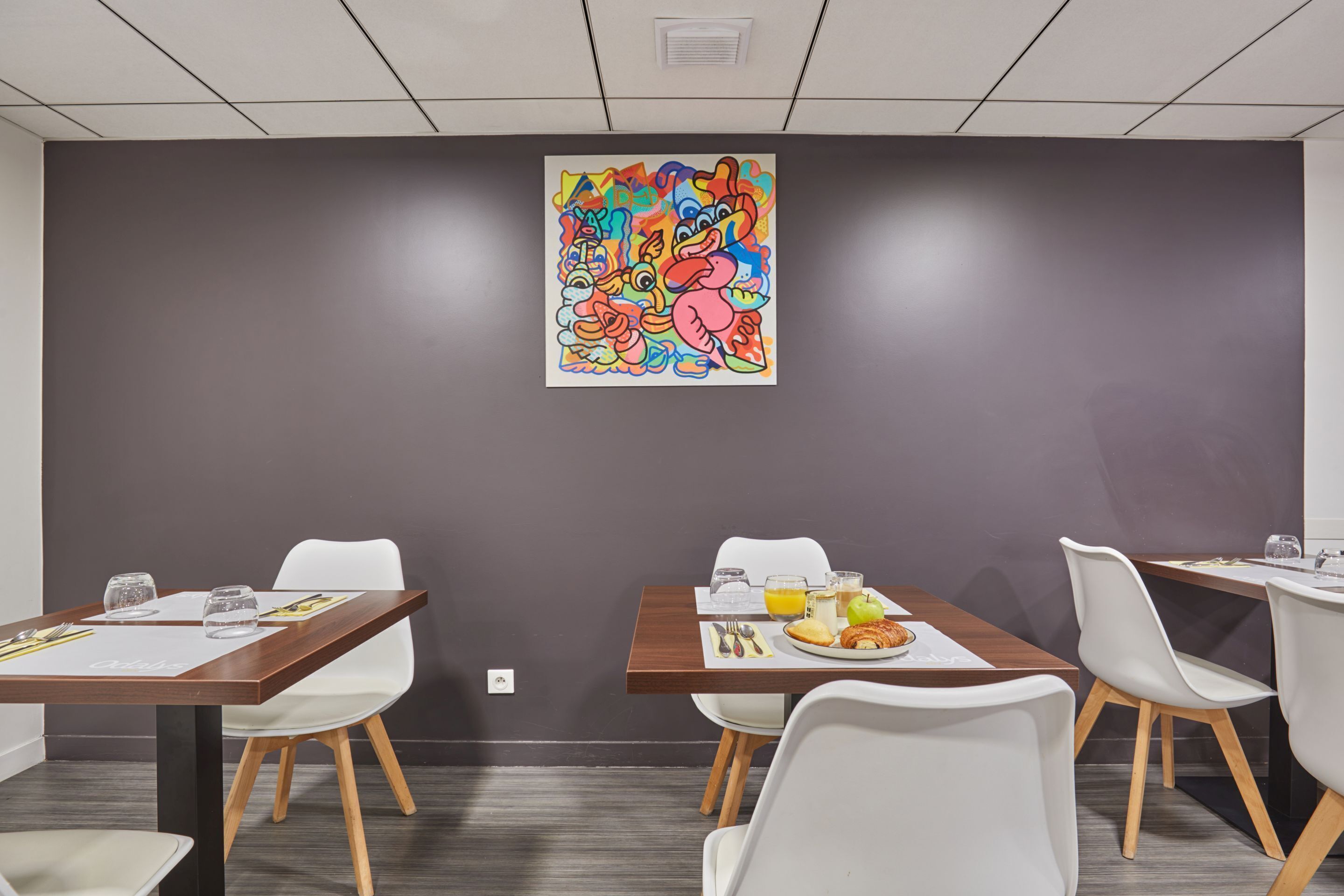A conference room with a large abstract painting, white chairs, and a table set with breakfast.