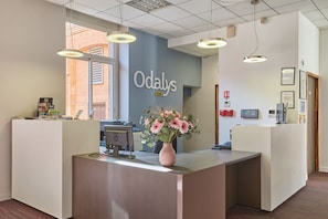 Eine Rezeption mit einem Blumenstrauß, einem Schild mit der Aufschrift 'Odaly's City' und einem Feuerlöscher an der Wand.