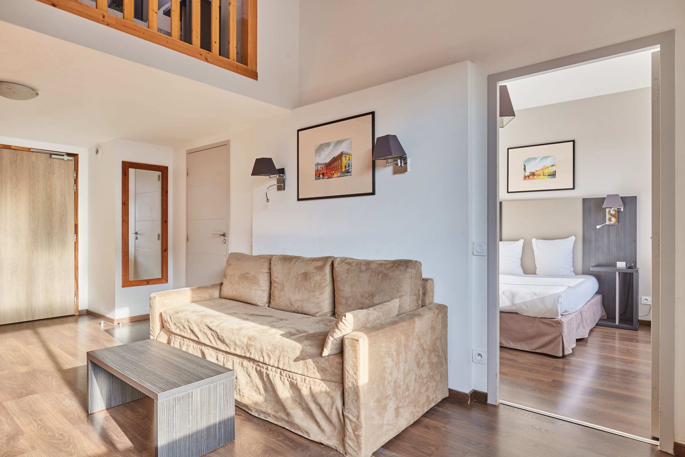 A modern living room with a sofa, a coffee table, and a bed in the adjacent room.