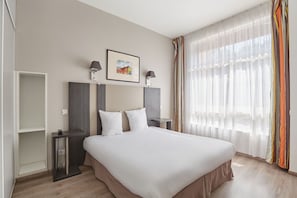 Ein Hotelzimmer mit Bett, Nachttischen, einem Wandbild in einem Rahmen und durchsichtigen Vorhängen.