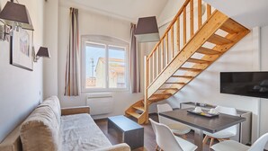 A modern living space with a sofa, dining table, chairs, a staircase, and a TV. - Odalys City Apartment Hotel - Toulouse Centre Gare (Toulouse)