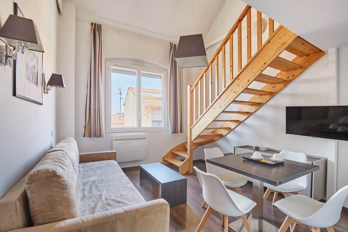 Ein zeitgemäßer Wohnraum mit Sofa, Esstisch, Stühlen, einer Treppe und einem Fernseher.