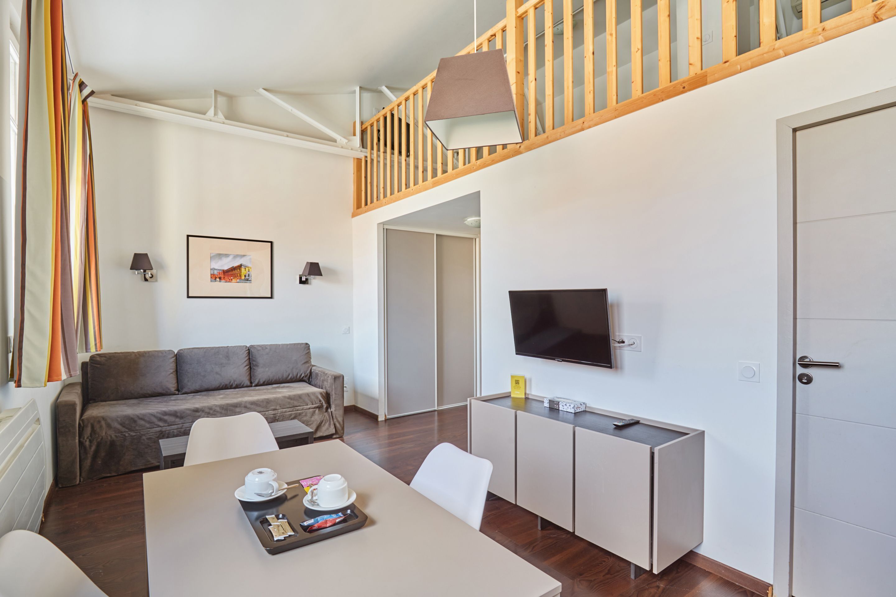A modern hotel room with a sofa, dining table, TV, and a staircase.